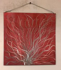 a red and silver metal wall hanging on the side of a white wall with an abstract tree design