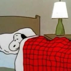 a dog laying in bed under a red and white blanket next to a green lamp