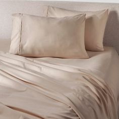 a bed covered in beige sheets and pillows