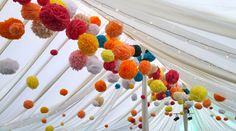 many colorful pom poms hanging from the ceiling in a white tent with string lights