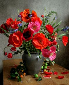 a vase filled with red and pink flowers on top of a wooden table in front of a gray wall