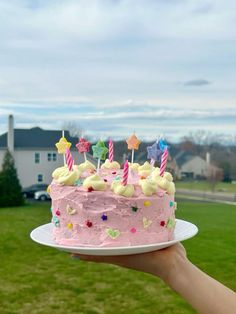 a hand holding a cake with pink frosting and candles