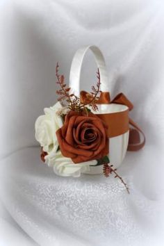 an orange and white flower arrangement in a basket on a white cloth covered tablecloth