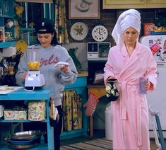 two women standing in a kitchen one holding a blender and the other wearing a robe