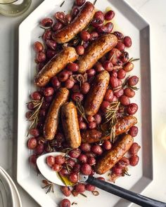 sausages and grapes on a white plate with a serving utensil next to them