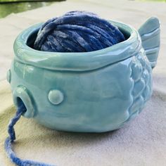 a ball of yarn in a blue bowl on a tablecloth with a thread spool