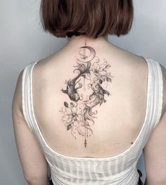 the back of a woman's neck with a fish and flowers tattoo on it