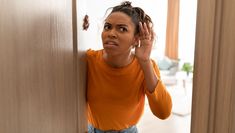 a woman in an orange shirt is leaning against a door and looking at the camera