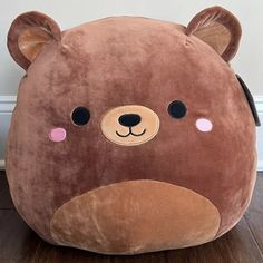 a large brown teddy bear pillow sitting on top of a wooden floor next to a wall