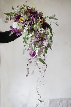 a woman holding a bouquet of flowers in her hand with purple and white blooms hanging from it