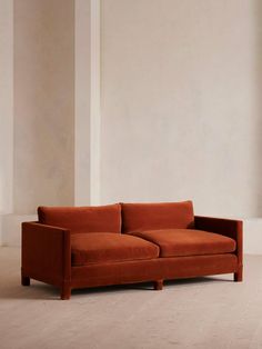 an orange couch sitting on top of a hard wood floor next to a white wall