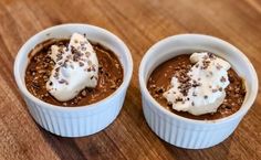 two small white bowls filled with food on top of a wooden table