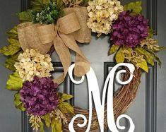 a monogrammed wreath with purple and yellow flowers is hanging on the front door