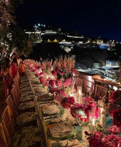 a long table is set up with candles and flowers for an outdoor dinner party overlooking the city at night