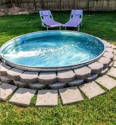 an empty swimming pool with two lawn chairs in the back ground and grass around it