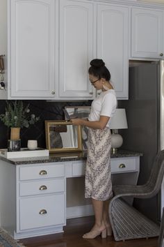 a woman standing in front of a kitchen counter with a mirror on top of it