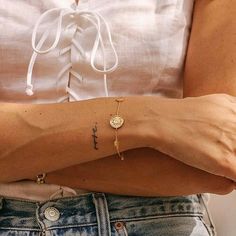 a woman's arm with a cross on it and a coin bracelet attached to the wrist