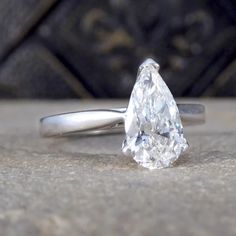 a white gold ring with a pear shaped diamond in the center, on top of a stone surface