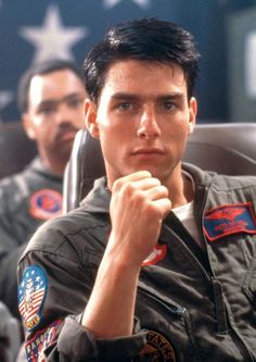 the young man is sitting in front of an american flag and looking off into the distance