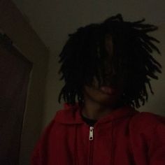 a young man with dreadlocks standing in the dark wearing a red hoodie