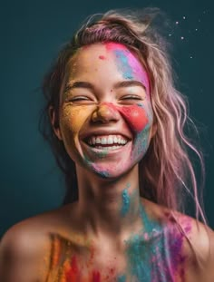 a woman with colorful paint on her face and chest smiles at the camera while she is covered in multi - colored powder