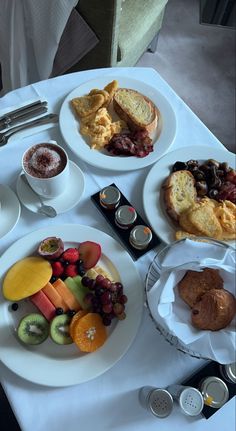 a white table topped with plates and bowls of food next to cups filled with fruit