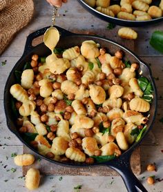 a skillet filled with pasta and chickpeas being drizzled with sauce