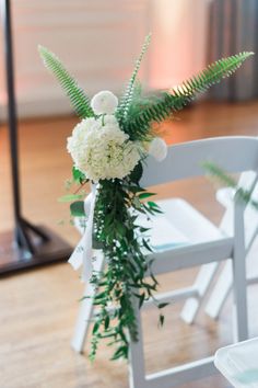 white flowers and greenery sit on the back of a chair at a wedding ceremony