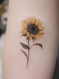 a small sunflower tattoo on the left side of the leg, it is yellow and has green leaves