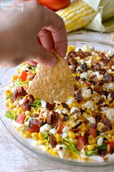 a person dipping a tortilla chip into a bowl full of corn and vegetables