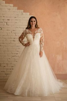 a woman in a wedding dress standing against a brick wall with her hands on her hips