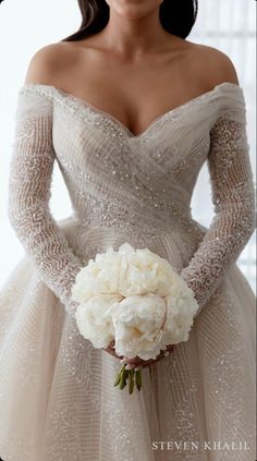 a woman in a wedding dress holding a bouquet of white flowers and wearing gloves with her hands on her hips