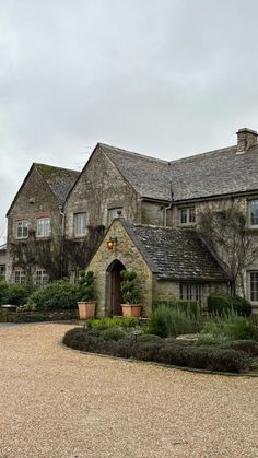 a large stone house with lots of trees and bushes around it's front entrance