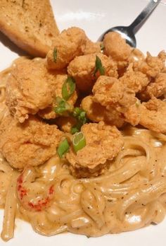 a white plate topped with pasta and fried chicken next to a slice of toasted bread