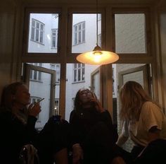 three women sitting in front of a window with their cell phones up to their mouths