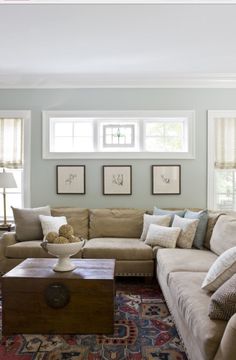 a living room filled with furniture and pillows on top of a carpeted floor next to two windows