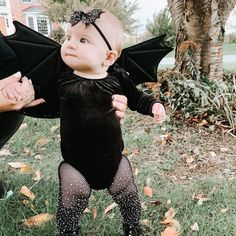 a baby dressed up as a bat standing in the grass