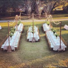 an outdoor wedding setup with white tablecloths and lights strung from the ceiling, surrounded by greenery