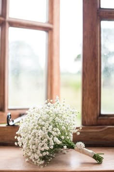 a bouquet of baby's breath sits on a table in front of two windows