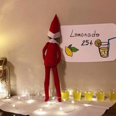 an elf is standing next to a sign with lemonade on it and glasses in front of him