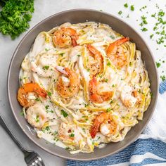 pasta with shrimp and cream sauce in a bowl on a blue towel next to parsley