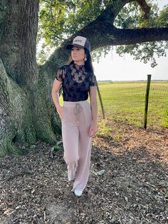 a woman standing in front of a tree wearing pink pants and a black top with lace on it