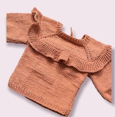 an orange sweater with ruffles on the shoulders is laying on a white surface