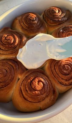 a bowl filled with cinnamon rolls and a spoon in the middle, sitting on a table