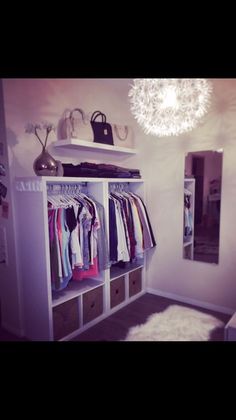 a white closet filled with lots of clothes next to a mirror and lamp hanging from the ceiling