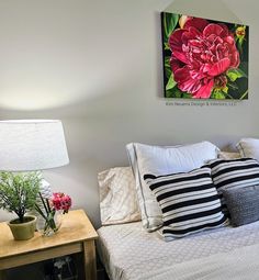 a bed with white sheets and black and white pillows next to a painting on the wall