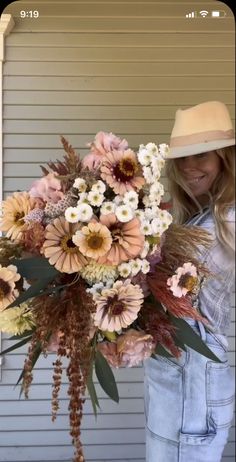 a woman holding a large bouquet of flowers in front of her face and wearing a hat