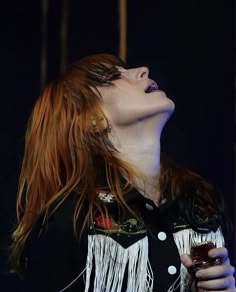 a woman with red hair and fringes on her shirt is singing into a microphone