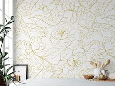 a white table topped with a vase filled with flowers next to a wall covered in gold foil