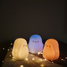 three little birds sitting on top of a wooden table next to some string lights in the dark